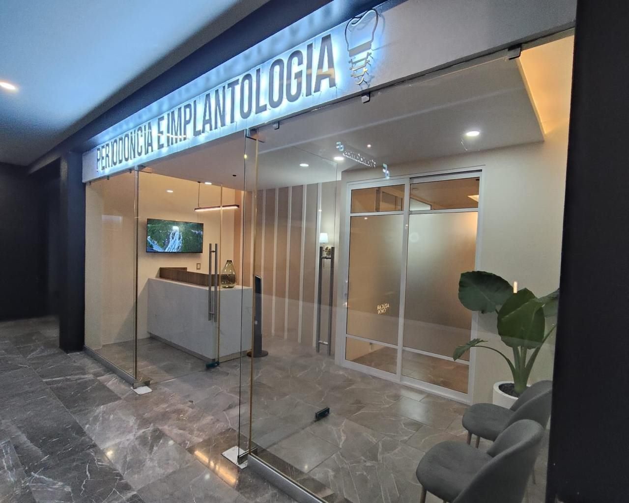 Entrada del consultorio de periodoncia e implantología en Plaza Sauce, Zamora, de noche y con el rótulo iluminado
